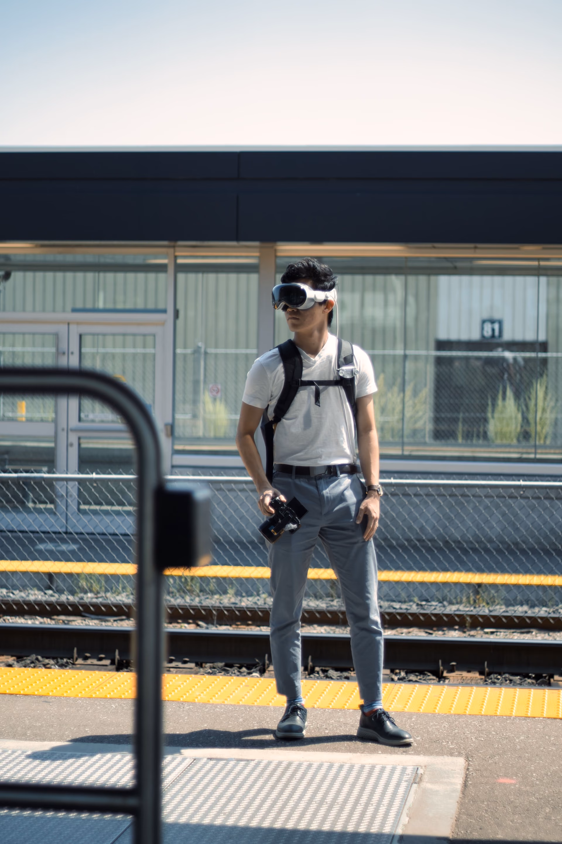 William Chai stands on a train platform wearing a visor and carrying camera equipment.