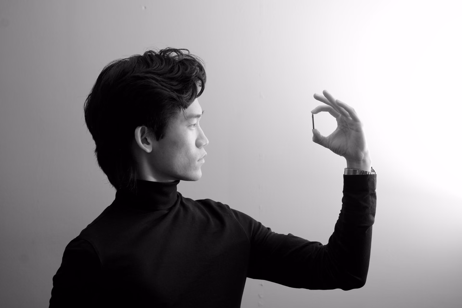 William Chai as Quinten holds a chip in a monochrome portrait.