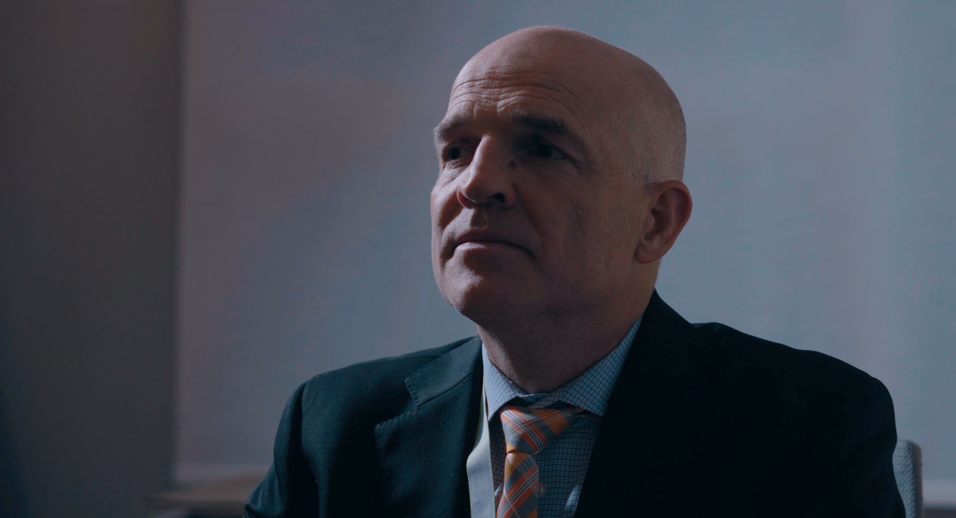 A man in a suit looks upward in Murder of Minus
